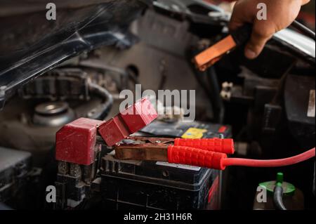 El mecánico conecta las abrazaderas a la batería descargada del vehículo. Foto de stock