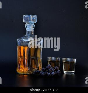 Grappa, una bebida alcohólica fuerte hecha de uvas negras en una botella de vidrio y dos vasos sobre fondo negro. Primer plano. Foto de stock