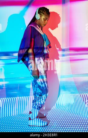 Vista lateral del joven joven milenio dominicano de moda con largas trenzas afro en el suelo y mirando hacia abajo mientras escucha música en la cabecera Foto de stock