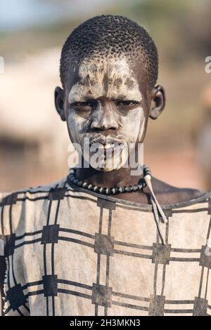 TRIBU MUNDARI, SUDÁN DEL SUR - 11 DE MARZO de 2020: Adolescente con ropa tradicional y con cara pintada con barro mientras vive en Mund Foto de stock