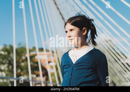 Retrato de niña de pie con líneas de puente sobre el fondo en el día soleado. Niño con vistas a la ciudad Foto de stock