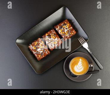 Brownie casero y tazas de cappuccino del café en la mesa oscura. Vista superior. Foto de stock