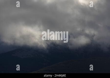 Vista de la montaña Moncayo, oscura, a la luz de la fría puesta de sol, cubierta de nubes, vista desde el pequeño pueblo de Litago Foto de stock