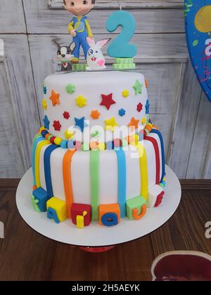 Hermoso pastel de cumpleaños, blanco con decoraciones coloridas, dos pisos  y un niño en miniatura con una vela de 2 años en la parte superior  Fotografía de stock - Alamy