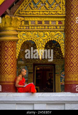 Luang Prabang, Laos - 4th de febrero de 2018: Un joven monje descansa contra una columna decorada mientras estudiaba en Wat Xieng Mouane
