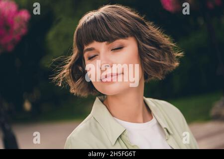 Retrato de atractiva alegre chica de pelo marrón soñadora pasar el día soleado olor aroma disfrutar de jardín floreciente al aire libre Foto de stock