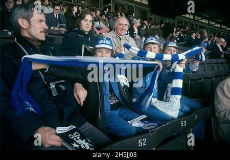 Londres 1982. Tres niños en foco durante un partido de fútbol. Son visiblemente fans de Chelsea con pañuelos y sombreros azules y blancos. Crédito Roland Palm. Foto de stock