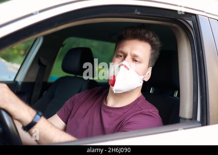 Un hombre conduciendo un coche en un respirador médico durante un brote de coronavirus, un taxista en una máscara, protección contra el virus. Conductor en coche blanco, mano