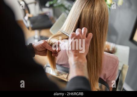 Pofessional peluquería está peinando un pelo de hermosa mujer blanca rubia en el salón moderno Foto de stock