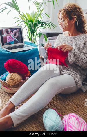 Mujer moderna hacer hobby Relájate la actividad de ocio en casa con trabajo de lana de punto y video tutorial en línea en el ordenador portátil y páginas web. Mujeres en h Foto de stock