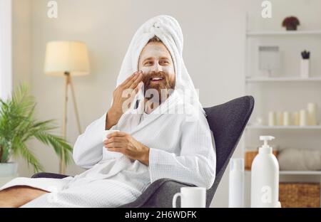 Hombre hispano vestido con maquillaje con gorro de toalla de ducha y  albornoz con una sonrisa feliz y fresca en la cara persona afortunada