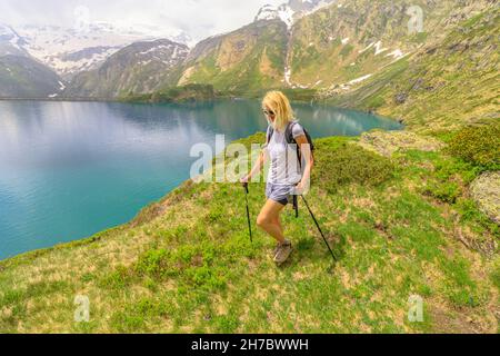 mochilero mujer turística trekking con postes frente al lago del lago Robiei y su presa. Embalse suizo en el valle de Maggia del cantón de Ticino. Parte superior de Foto de stock