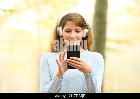 Vista frontal retrato de una mujer escuchando música con auriculares y comprobando el teléfono en un parque Foto de stock