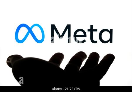 Facebook META Plataformas logotipo de la empresa visto en la pantalla de fondo borrosa y silhuette de mano abierta en frente de ella. Concepto. Stafford, Reino Unido, N