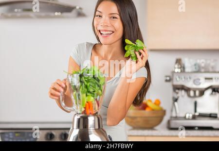 Batido verde sano mujer asiática usando espinacas en la licuadora para hacer jugo de verduras desintoxicadas en casa. Sonriente joven cocinando
