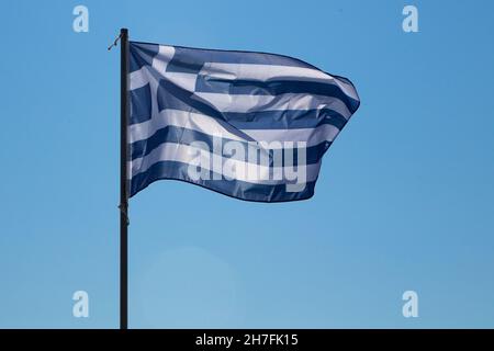 Bandera nacional de Grecia que revolotean en el viento en un asta de bandera. Aislado contra un cielo azul brillante. Foto de stock
