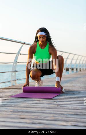 Atleta joven poniendo colchoneta de yoga en una caminata ancha Foto de stock