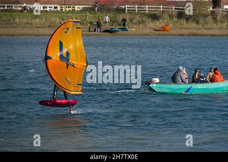 Persona en un ala de aluminio a velocidad pasando un pequeño barco por el río Adur en Shoreham. Foto de stock