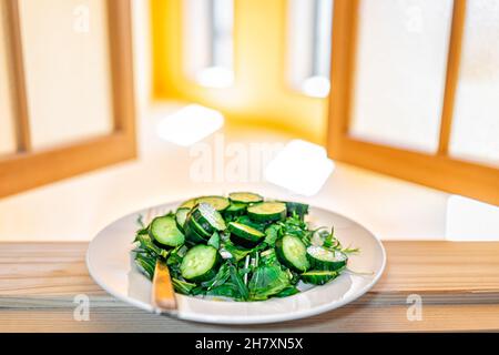 Ventana japonesa tradicional abierta amarilla con luz del sol con primer plano de plato de verduras ensalada de color verde plato macro con pepinos japoneses y verduras mizuna Foto de stock