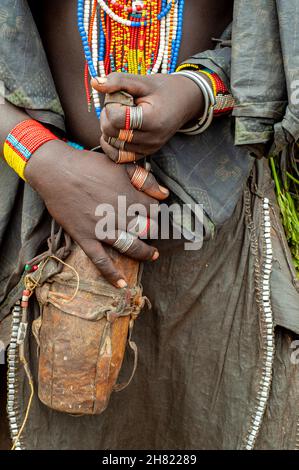 mujer joven sosteniendo un recipiente para líquido hecho de madera, con coloridos collares de cuentas y aros de alambre de cobre y medalla Foto de stock