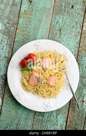 Porción de espaguetis con albahaca, tomates y pescado rojo sobre mesa de madera vieja vertical Foto de stock