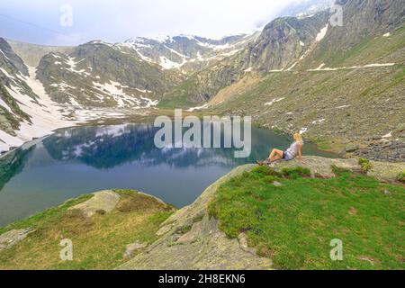 Embalse suizo en el Valle de Maggia del cantón Ticino de Suiza con Cavagnoo dan. Mujer turística descansando durante el trekking alrededor del Lago Bianco Foto de stock