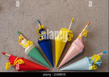 seis coloridos conos de azúcar pequeños rellenos para volver a la escuela dispuestos en un semicírculo sobre un fondo gris Foto de stock