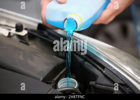 Un hombre vierte anticongelante de un recipiente a un motor de coche Foto de stock