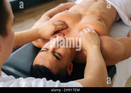 Vista de primer plano de la espalda del masajista profesional masculino con manos fuertes que masajean los músculos del hombro y el pecho del atleta muscular después del entrenamiento deportivo Foto de stock