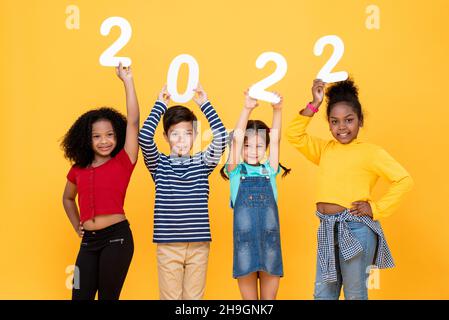 Felices y lindos niños pequeños sonriendo y sosteniendo 2022 números aislados sobre fondo amarillo del estudio para los conceptos de año nuevo