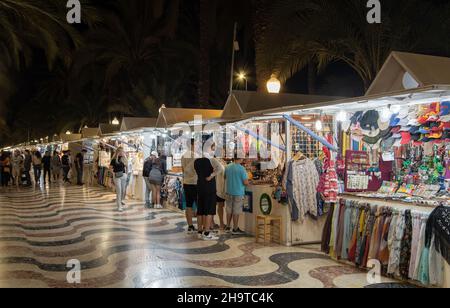 Pareja, hombres y mujeres caminando y mirando artículos en los puestos de venta de artesanías en el mercado nocturno de la Esplanada de España en Alicante, España