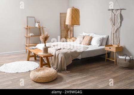 Jarrón con pampas sobre banco de madera cerca de cama doble Foto de stock