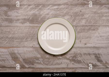 Vista superior Imagen de placa metálica esmaltada blanca con borde verde sobre mesa de madera gris Foto de stock