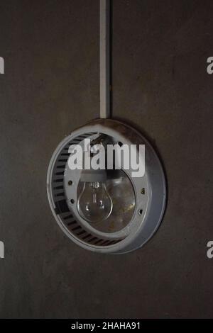 Una lámpara apagada de una lámpara de forma redonda sin una plafond colgando en la pared en una habitación oscura. Foto de stock