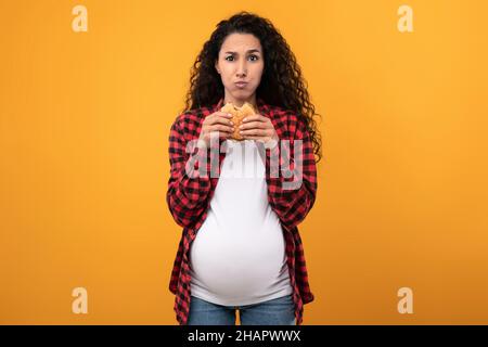 Embarazada Señora sosteniendo comer hamburguesa en el estudio