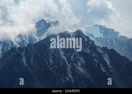 Picos nevados de montaña con nubes en un día soleado Foto de stock