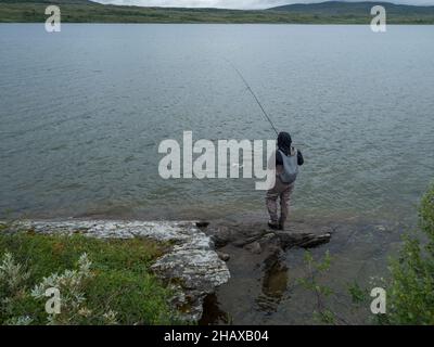 Pescador pescador pescador pescador en la orilla del lago pesca con mosca y pesca truchas o peces carboneros en el lago Gieddavrre en Suecia Laponia en la ruta de senderismo Padjelantaleden.