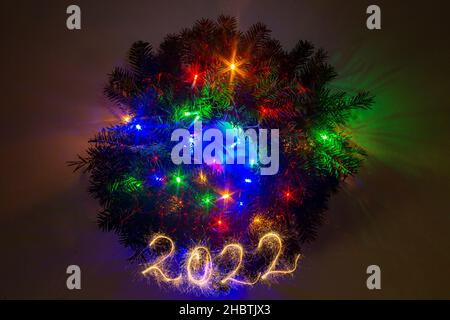 Corona de abeto de Navidad multicolor brillando en la oscuridad, con 2022 escritos con gorriones.