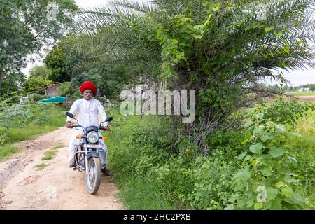Jawai, Rajasthan, India - septiembre de 2021: Retrato de un anciano del grupo étnico rabari en un tocado nacional y blanco tradicional en bicicleta. Foto de stock