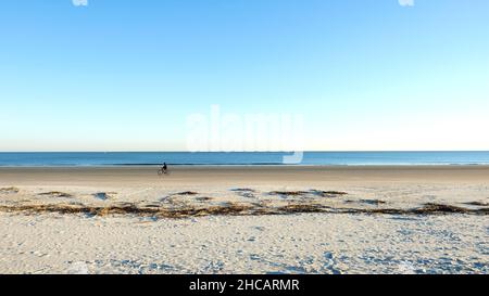 Un solo ciclista en una solitaria franja de playa de arena clara en Hilton Head, Carolina del Sur, Estados Unidos; diversión, ejercicio y relajación en un día soleado.