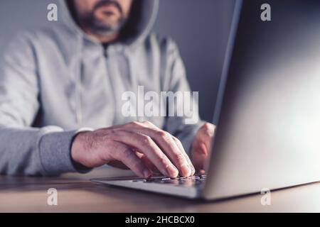 Concepto de hacker de sombrero gris, hombre trabajando en el portátil para descubrir debilidades en la red de computadoras, enfoque selectivo Foto de stock