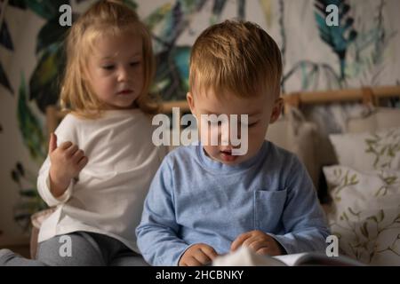 Un chico lindo con un libro y una hermana gemela en el dormitorio de la casa