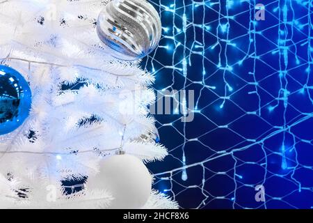 Árbol de Navidad artificial blanco decorado con bolas sobre el fondo de las luces azules de Navidad. Foto de stock