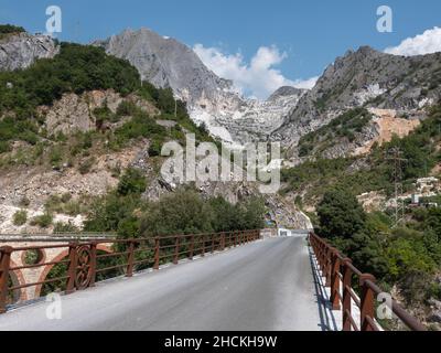En un puente: Vista de una montaña en Carrara en verano con rocas cubiertas de vegetación y árboles. Foto de stock