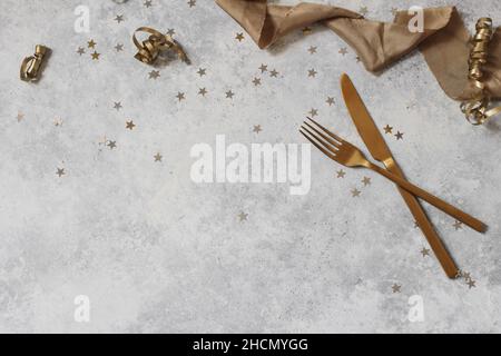 Composición de Año Nuevo con estrellas de confeti de oro, cuchillo de mesa, tenedor y cintas de seda. Decoración de fiesta, concepto de celebración. Capa plana, superior Foto de stock