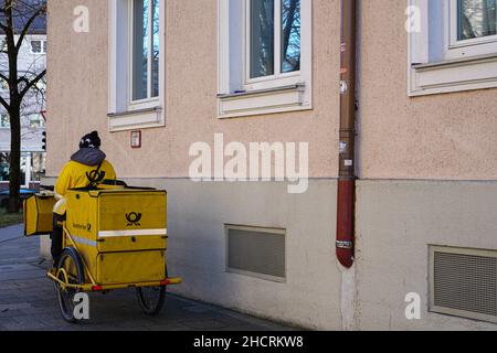Un cartero de DHL toma un descanso. Él está sentado en su bicicleta amarilla con un remolque de contenedor que sostiene el correo diario para su área.