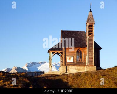 Por la mañana vista de la pequeña iglesia de madera o capilla en la cima de la montaña Col di lana y el Monte Marmolada, Alpes Dolomitas montañas, Italia Foto de stock