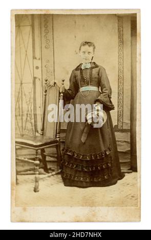 Original Victorian CDV estudio retrato de mujer joven o, lo más probable, una adolescente sosteniendo un bonete, azul mano tinte de color añadido a la cintura y el cuello, que parece espinoso, ligeramente espeluznante fotografía. Alrededor de 1860, Reino Unido