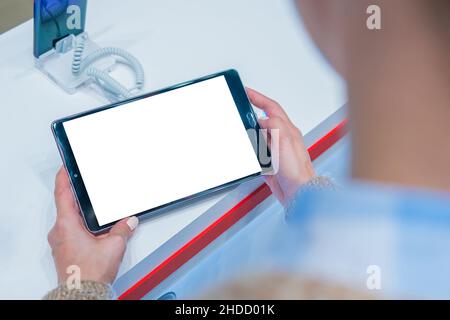 Maqueta: Mujer mirando la tableta con pantalla blanca en blanco en la tienda, tienda Foto de stock