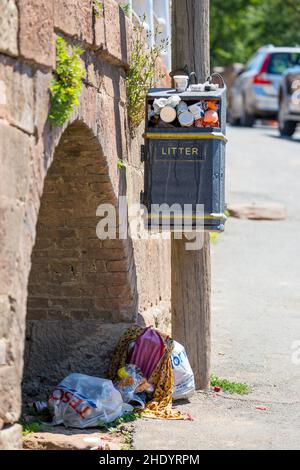 Contenedor de basura en un bello lugar del Reino Unido, lleno de basura desbordante y aún más bolsas de basura llenas de basura en el suelo. Foto de stock